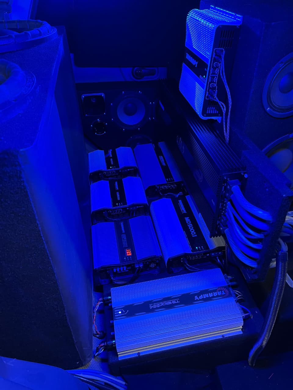 Car boot fitted with a bank of amplifiers and heavy power wiring under blue light