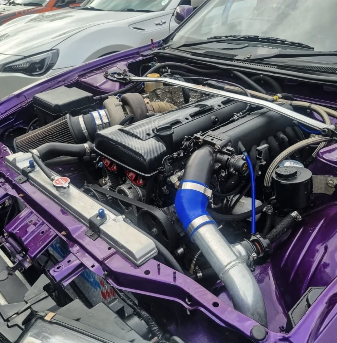 Open engine bay of a purple car with a turbocharged engine and blue intake piping